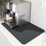 Stainless steel espresso machine on a white countertop with a black mat underneath.