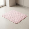 A light pink, square bath mat with a raised circular bubble texture, shown on a light beige speckled floor in a clean bathroom corner.