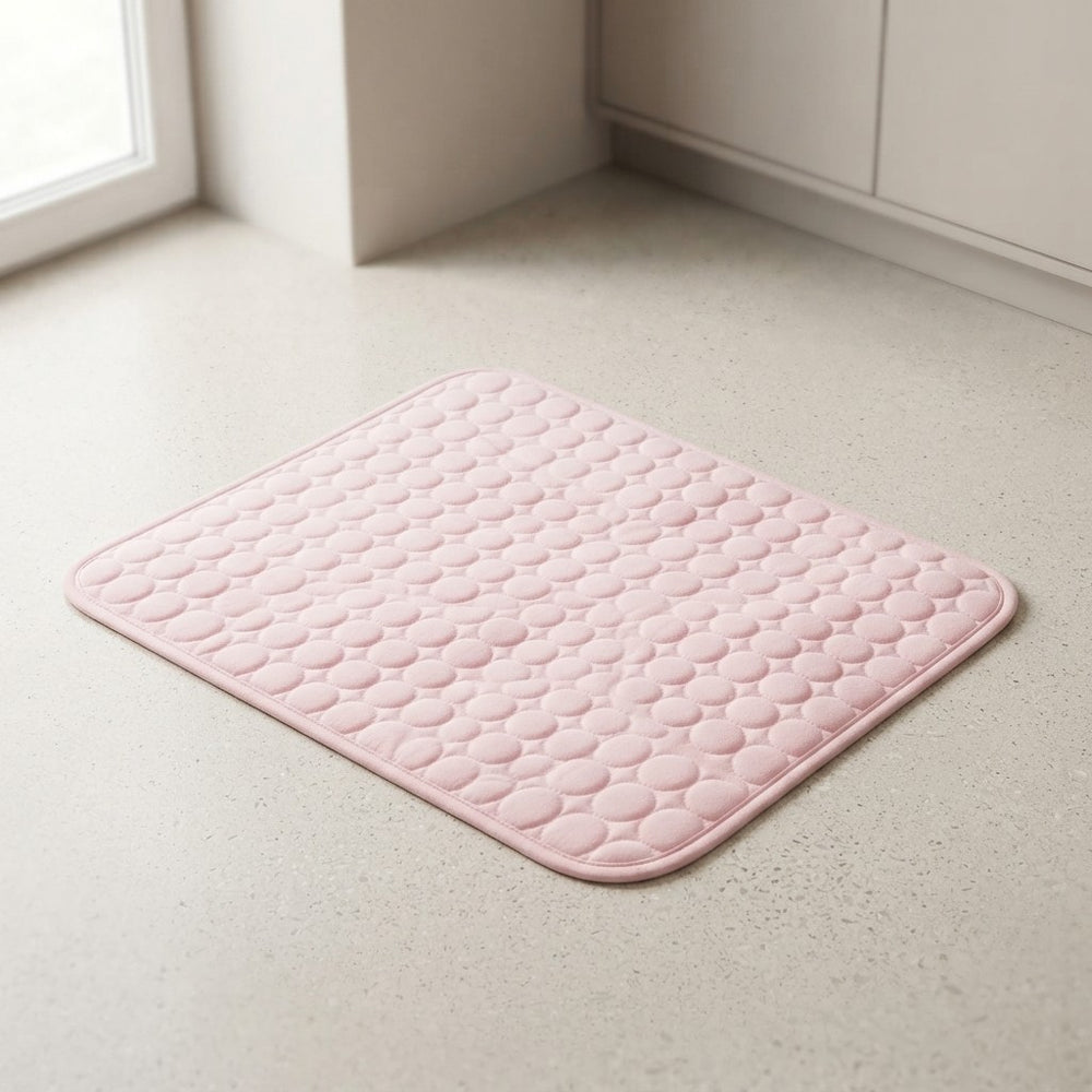 A light pink, square bath mat with a raised circular bubble texture, shown on a light beige speckled floor in a clean bathroom corner.