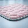 A close-up of a light pink quilted cooling mat with a gray stitched border, showing its textured mesh surface.